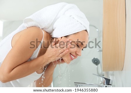 Happy mature woman washing face in bathroom