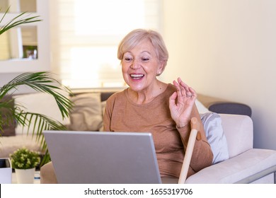 Happy Mature Woman Waving To Someone While Having A Video Call Over Laptop At Home. Gray-haired Senior Woman Waving Hand In Front Of Laptop While Having Video Call With Her Family Members.