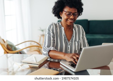 Happy Mature Woman Working On Laptop At Home Office. African Woman Sitting At Desk And Using Laptop At Home.