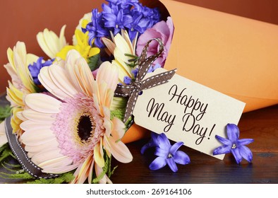 Happy May Day Traditional Gift Of Spring Flowers In Orange Paper Cone On Dark Wood Table. 