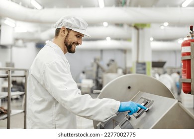 A happy meat factory laborer is pressing start button on a meat processing machine in facility. - Powered by Shutterstock