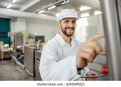 A happy meat industry inspector is checking on meat processing machine and holding tablet while smiling at display. - Powered by Shutterstock