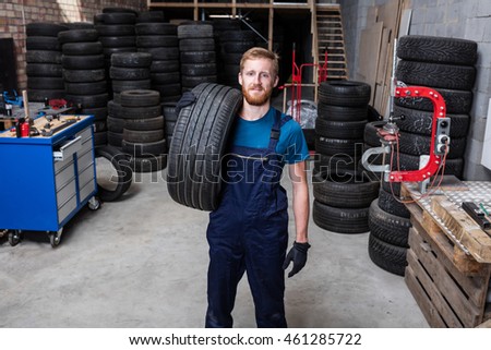 Happy mechanic carrying a tire in tire service.
