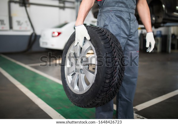 Happy mechanic\
carrying a tire in tire\
service.
