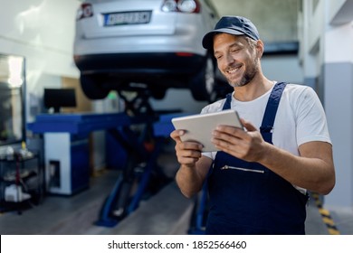 Happy Mechanic Using Digital Tablet At Auto Repair Shop.