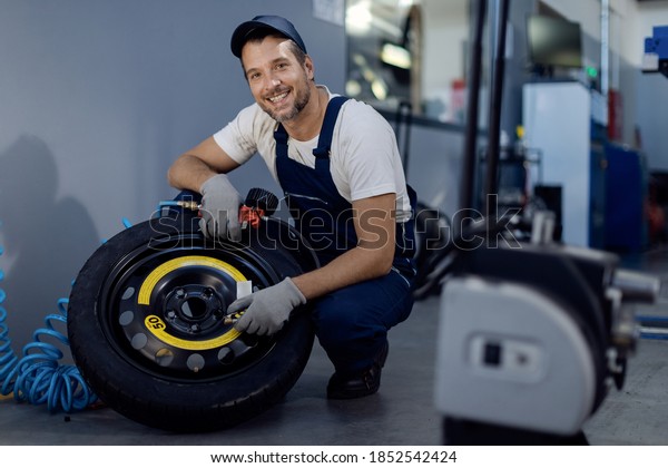 Happy mechanic using\
pressure gauge while repairing car tire in a workshop and looking\
at camera.