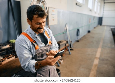 Happy mechanic using smart phone while working in a repair shop. Copy space. - Powered by Shutterstock