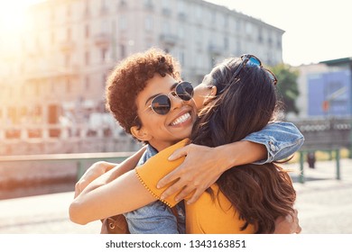 Happy meeting of two friends hugging in the street. Smiling girls friends laughing and hugging in the city centre. Multiethnic young women embrace each others after long time they have been distant.