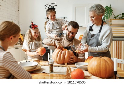 Happy Members Of Multi Generational Family With Pumpkins Gathering Around Table And Preparing For Halloween Celebration In Kitchen At Home
