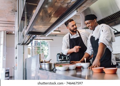 Happy men chefs cooking food at cafe kitchen. Two cooks making food dishes in restaurant kitchen. - Powered by Shutterstock