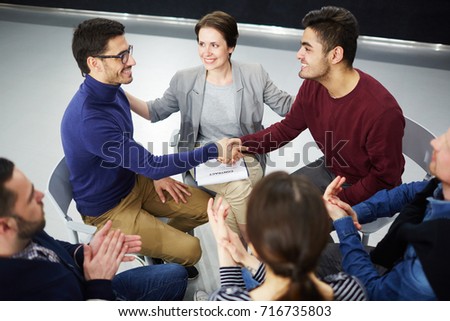Happy men handshaking with helpful psychologist and applauding colleagues near by