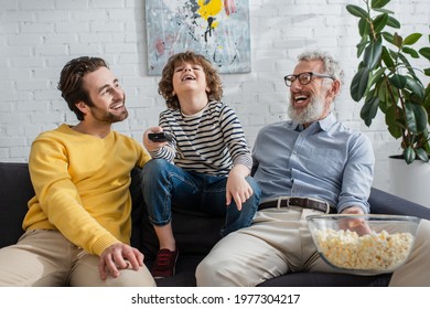 Happy men with popcorn sitting near child with remote controller