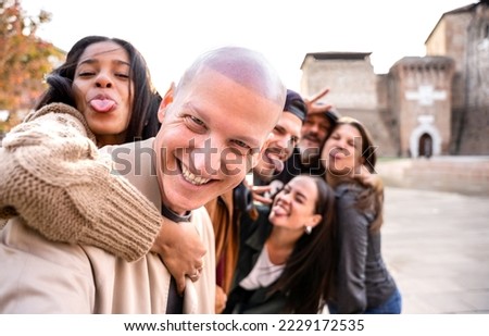 Happy men and women having fun together hanging out -Multicultural friends group taking selfie picture outdoors - Making strange face with tongue out - Focus on first guy