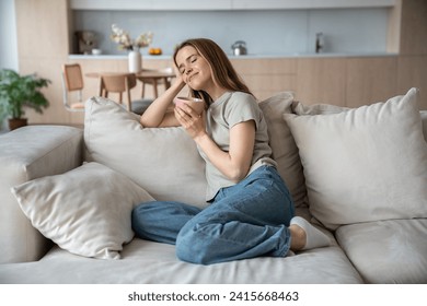 Happy merry middle-aged European woman sitting on comfortable sofa with eyes closed, dreaming, thinking of pleasant things, drinking hot tea, coffee, cocoa, smelling aroma, relaxing in cozy atmosphere - Powered by Shutterstock