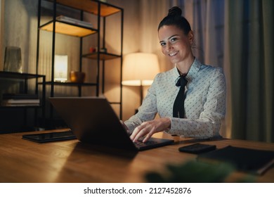 Happy mid adult business woman with diary working on laptop in office at night, looking at camera.