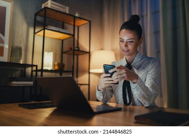 Happy mid adult business woman with diary working on laptop in office at night, looking at camera.
