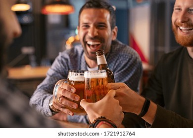 Happy Mid Adult Friends Clinking With Beer Mugs In Pub. Three Cheerful Guys Drinking Draft Beer, Celebrating Meeting And Smiling. Laughing Young Men Enjoying Cold Pint Of Beer During Night At Bar. 