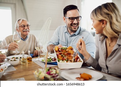 Happy Mid Adult Man Talking To His Wife While Passing Her Food During Family Lunch At Home. 