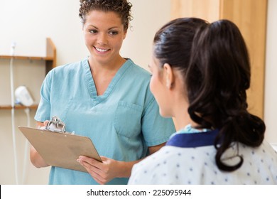 Happy Mid Adult Nurse With Clipboard Looking At Patient In Ultrasound Room