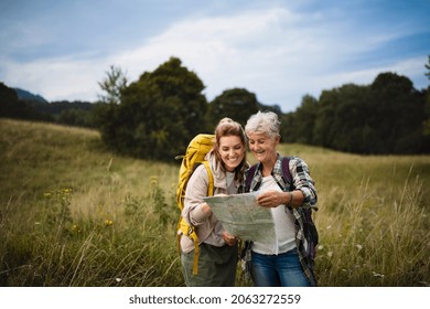 Happy Mid Adult Woman With Active Senior Mother Hiking And Looking At Map Outdoors In Nature.