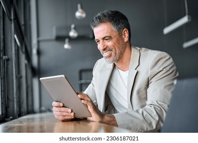 Happy mid aged business man wearing suit standing in modern office using digital tablet. Mature businessman professional manager holding tab working on financial data on fintech device. - Powered by Shutterstock