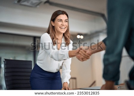 Happy mid aged business woman manager handshaking greeting client in office. Smiling female executive making successful deal with partner shaking hand at work standing at meeting table.