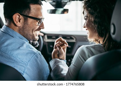 Happy Middle Age Couple Enjoying While Choosing And Buying New Car At Showroom. Rear View.