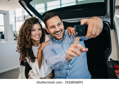 Happy middle age couple enjoying while choosing and buying new car at showroom. They making selfie photo with their new car.