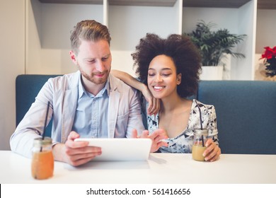 Happy Middle Age Interracial Couple Sitting In Cafe Bar, Smiling And Looking At White Tablet.