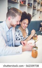 Happy Middle Age Interracial Couple Sitting In Cafe Bar, Smiling And Looking At White Tablet.