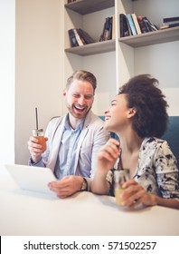 Happy Middle Age Interracial Couple Sitting In Cafe Bar, Smiling And Looking At White Tablet.