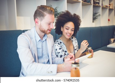 Happy Middle Age Interracial Couple Sitting In Cafe Bar, Smiling And Looking At White Tablet.