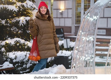 Happy Middle Age Woman Catching Snowflakes In The City Outdoors. Relaxed Emotional Person Walking In Winter Urban Area In A Moment, Slow Living, Sincere Authentic Life. Evening Lights