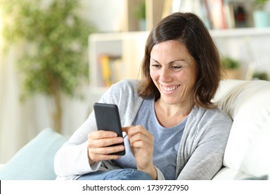 Happy Middle Age Woman Checking Smart Phone Sitting On A Couch In The Living Room At Home