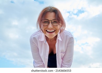 Happy Middle Age Woman Looking Down At Camera, Blue Sky In Clouds Background.