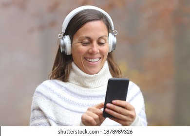 Happy Middle Age Woman Wearing Headphones Listening To Music On Smart Phone