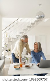 Happy Middle Aged 50s Family Couple Having Fun Using Laptop Computer And Talking At Home. Smiling Senior Older Mature Husband And Wife Laughing Distance Working Spending Time In Living Room.