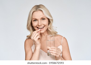 Happy middle aged 50s woman holding pill and glass of water taking dietary supplements. Portrait of smiling adult attractive woman taking care of health in menopause, isolated on white. - Shutterstock ID 1958672593