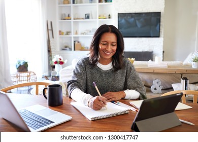 Happy middle aged African American woman sitting at table in her dining room making notes, selective focus - Powered by Shutterstock