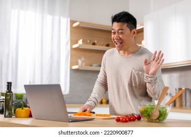 Happy Middle Aged Asian Man Cooking Dinner At Home, Having Video Conference With His Family, Attending Online Cooking Class, Using Laptop, Kitchen Interior, Copy Space. Cooking, Culinary Courses