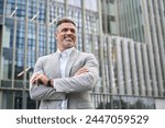 Happy middle aged business man ceo executive thinking of future success leadership, mature rich businessman manager lawyer in suit standing outside corporate buildings in city looking away. Copy space