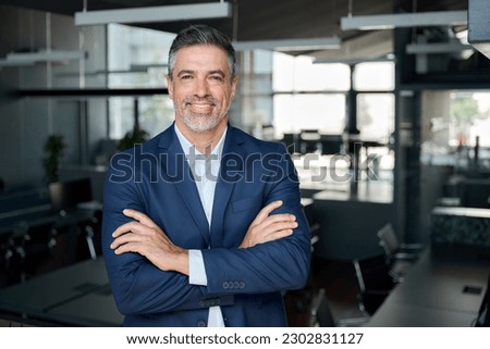 Happy middle aged business man ceo standing in office arms crossed. Smiling mature confident professional executive manager, proud lawyer, confident businessman leader wearing blue suit, portrait.