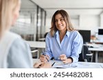 Happy middle aged business woman hr talking to recruit at job interview meeting. Smiling mature female financial advisor, professional bank manager consulting client working in corporate office.