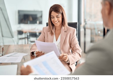 Happy middle aged business woman account manager discussing documents financial result project overview at office meeting, two professional executives holding tax papers consulting working together.