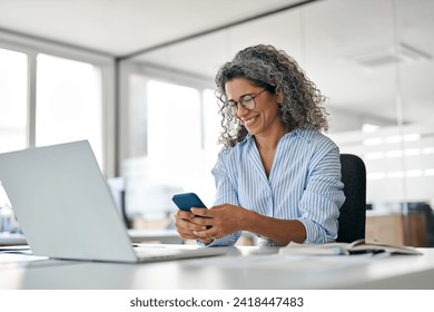 Happy middle aged business woman holding mobile cell phone using cellphone in office. Smiling mature older professional lady business owner entrepreneur using smartphone working sitting at desk. - Powered by Shutterstock