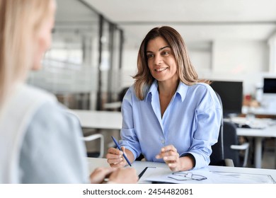 Happy middle aged business woman hr talking to recruit at job interview meeting. Smiling mature female financial advisor, professional bank manager consulting client working in corporate office. - Powered by Shutterstock