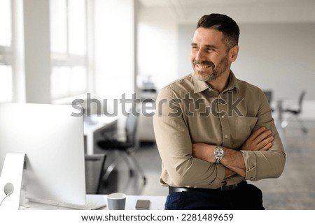 Happy middle aged businessman standing by his workplace, looking aside at copy space, thinking of new startup or project, smiling at good thoughts, planning investment, enjoying success