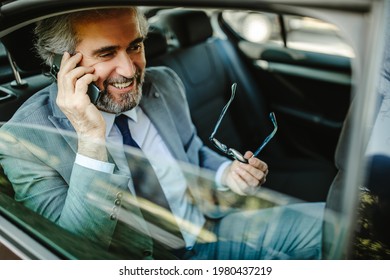 Happy middle aged businessman using cell phone in car, having phone call and holding glasses. - Powered by Shutterstock