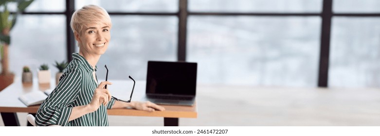 Happy Middle Aged Businesswoman Sitting At Laptop At Workdesk Smiling To Camera In Modern Office. Panorama With Copy Space - Powered by Shutterstock