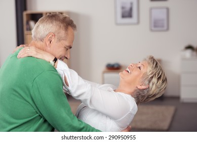 Happy Middle Aged Couple Dancing At The Living Room While Holding Each Other And Laughing.